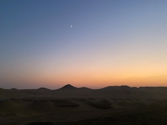 A peaceful desert scene at dusk with soft orange and rose pale hues blending into the horizon.