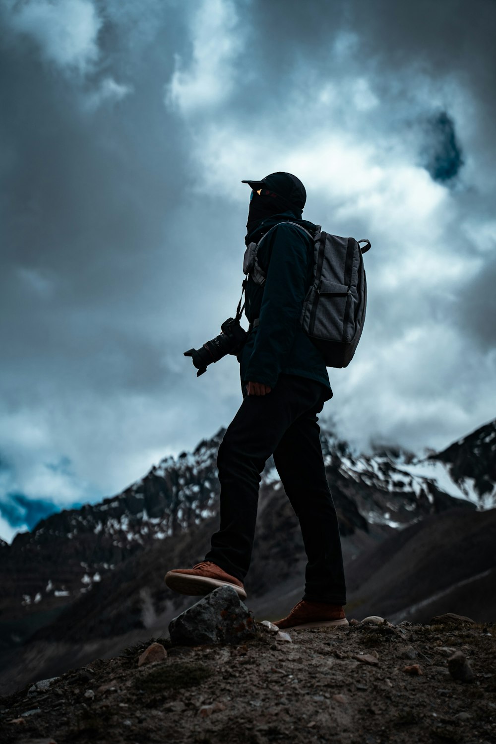 man in black jacket and black pants with black backpack standing on rock formation under gray