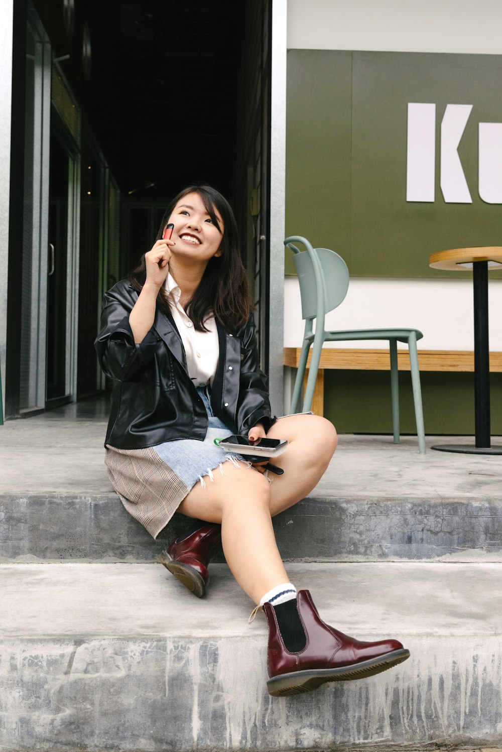 woman in black leather jacket and red skirt sitting on concrete bench