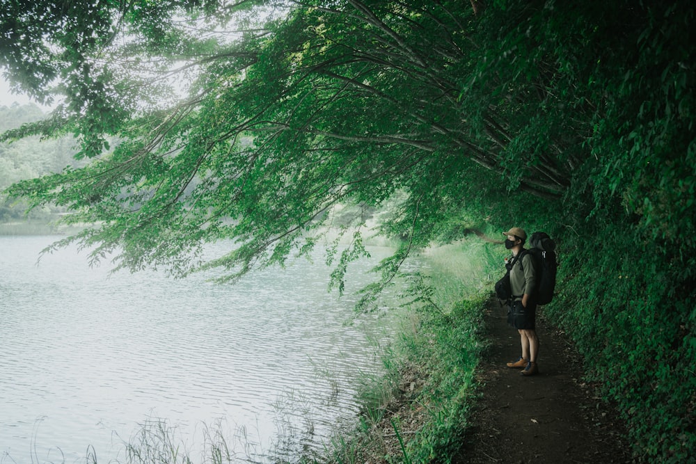 Mujer en vestido negro de pie sobre hierba verde cerca del cuerpo de agua durante el día