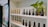 Shelves display an array of nail polish bottles arranged neatly. Various brands and shades are visible, including some with black, gold, and white labels. A small green houseplant adds a touch of nature to the setting, creating an inviting atmosphere. The background features a decorative floral pattern.