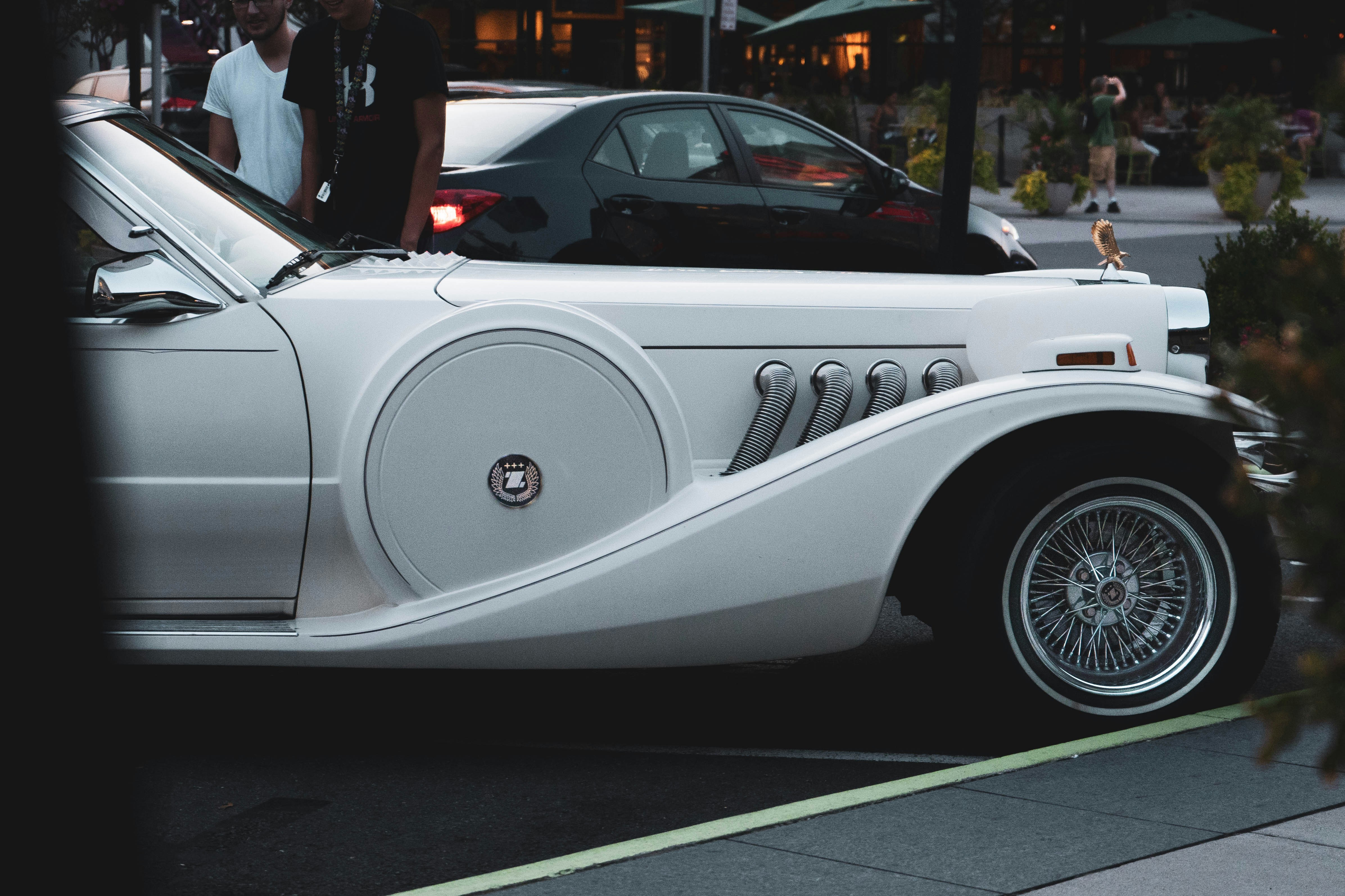 man in black jacket standing beside white convertible coupe during daytime