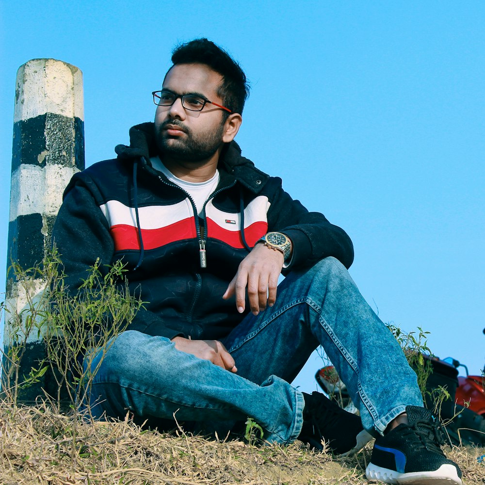 man in black and red zip up jacket sitting on brown rock