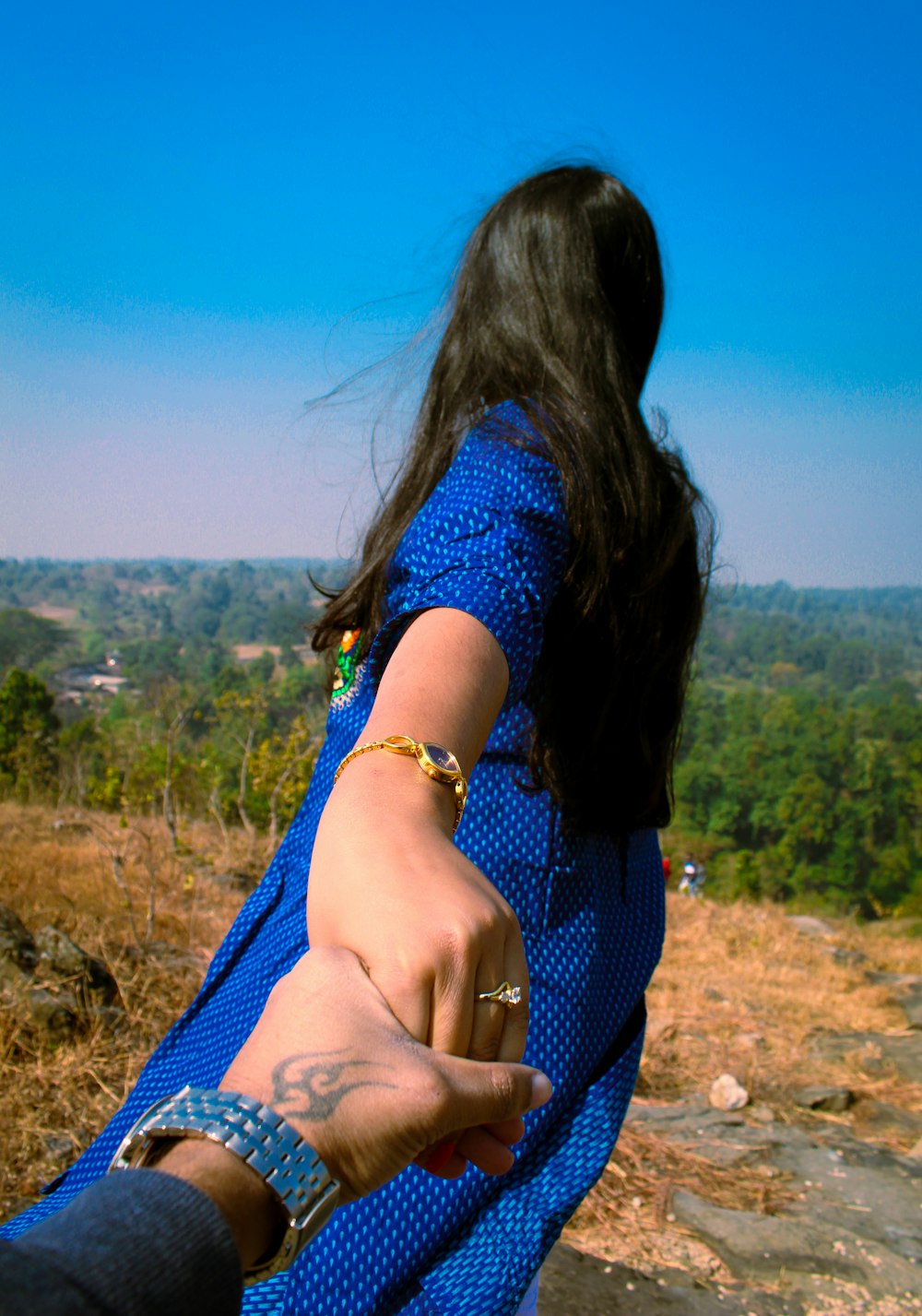 Femme en robe à fleurs bleue et blanche assise sur le champ d’herbe brune pendant la journée