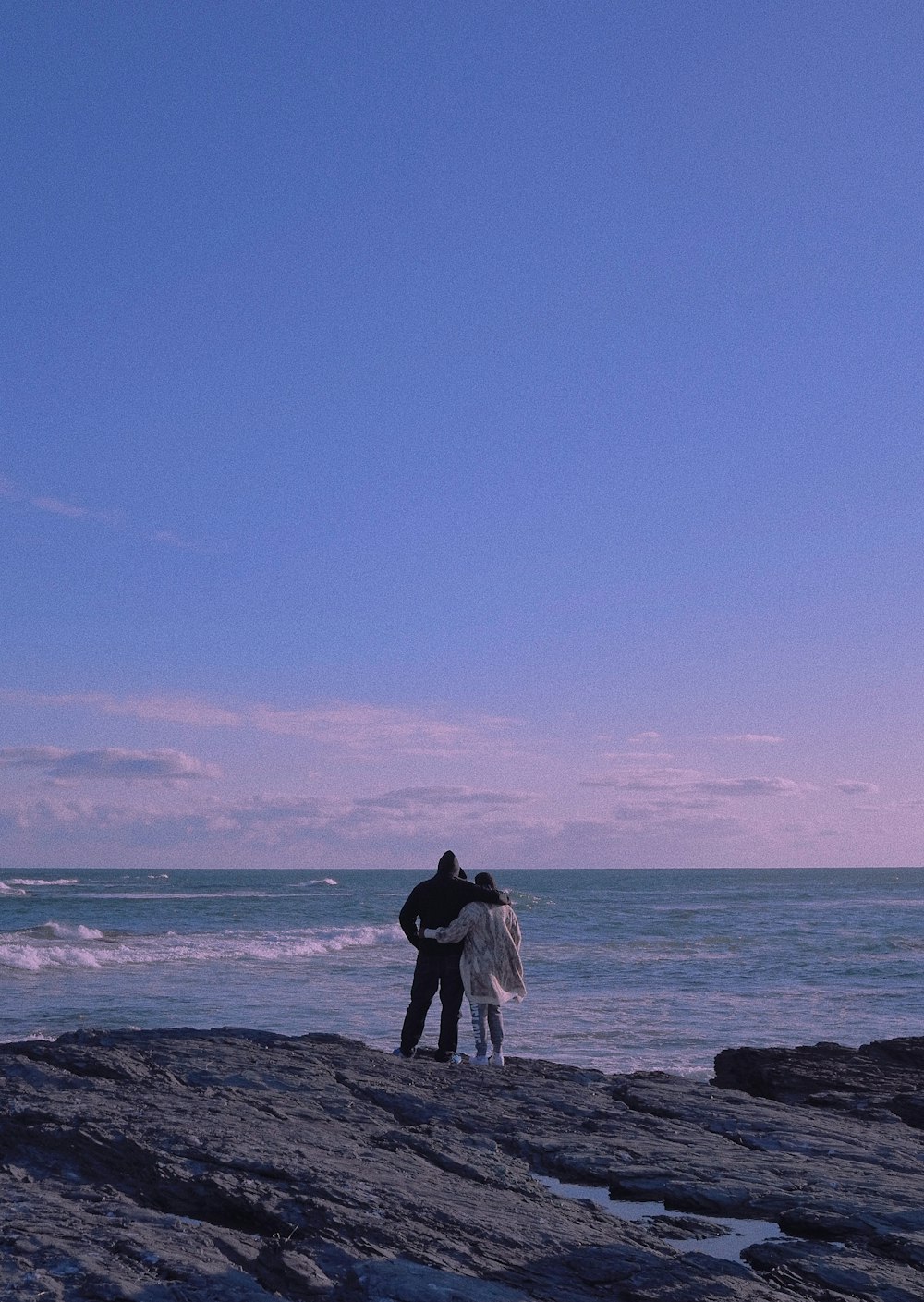 couple standing on rocky shore during daytime