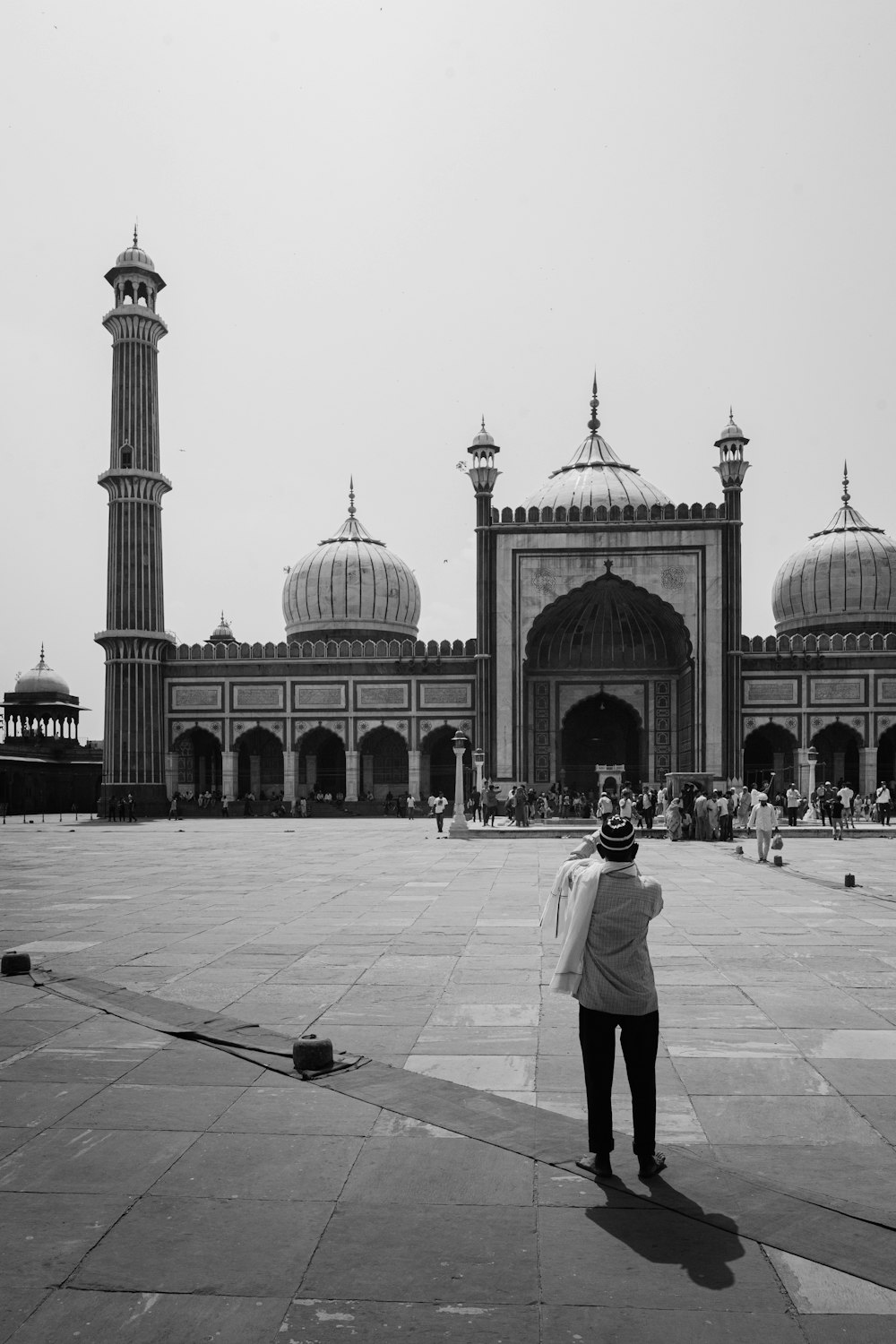 grayscale photo of man in white long sleeve shirt and black pants standing near mosque