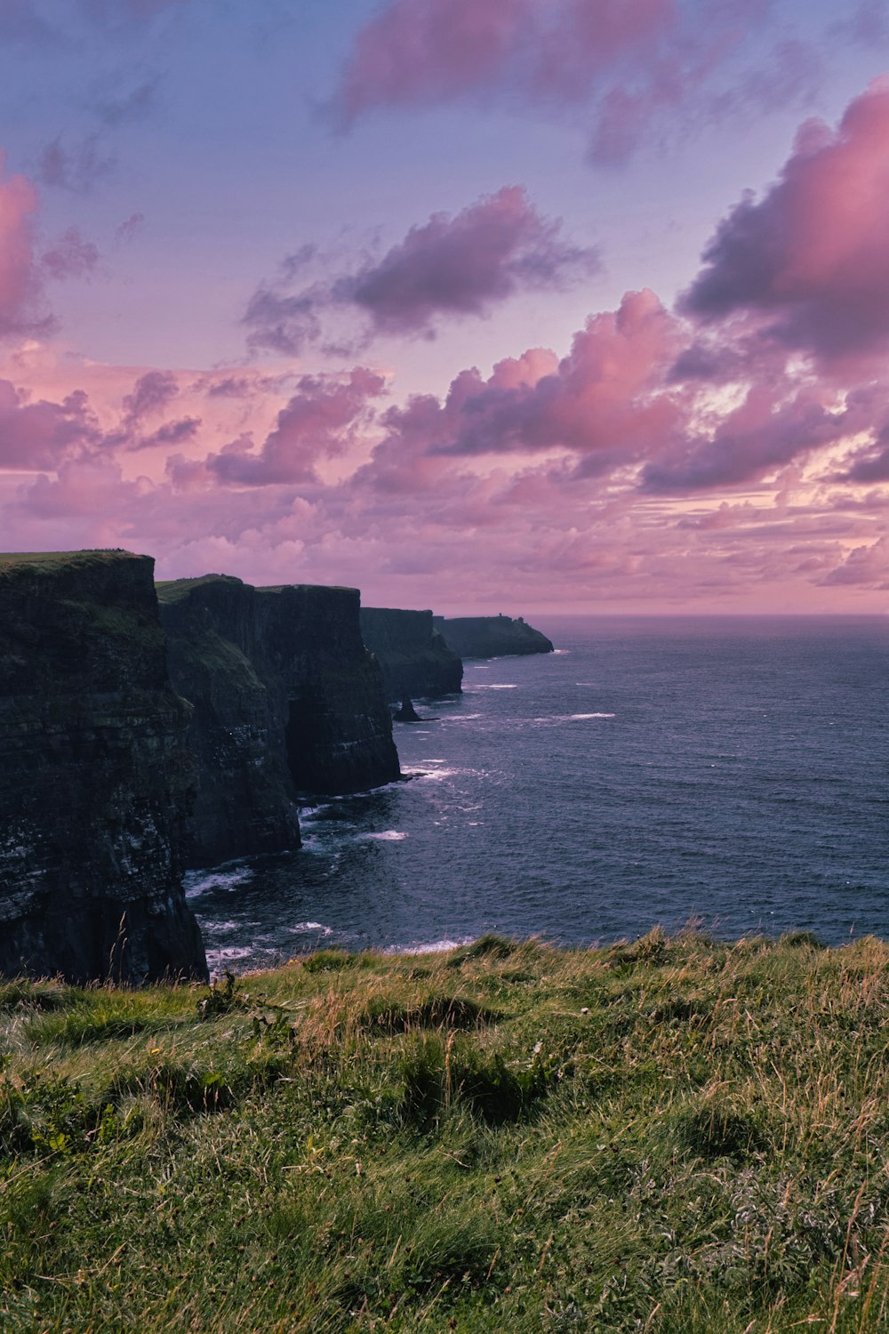 green grass on cliff by the sea under cloudy sky during daytime