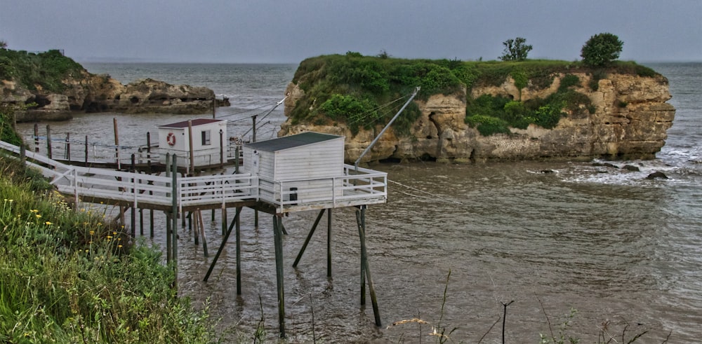 white wooden house on brown rock formation beside body of water during daytime