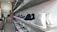 A shoe store with multiple shelves displaying a variety of sneakers. The shelves are arranged in a neat and organized manner with sneakers in different colors and styles. A person is seated at a counter in the background, possibly a store employee.