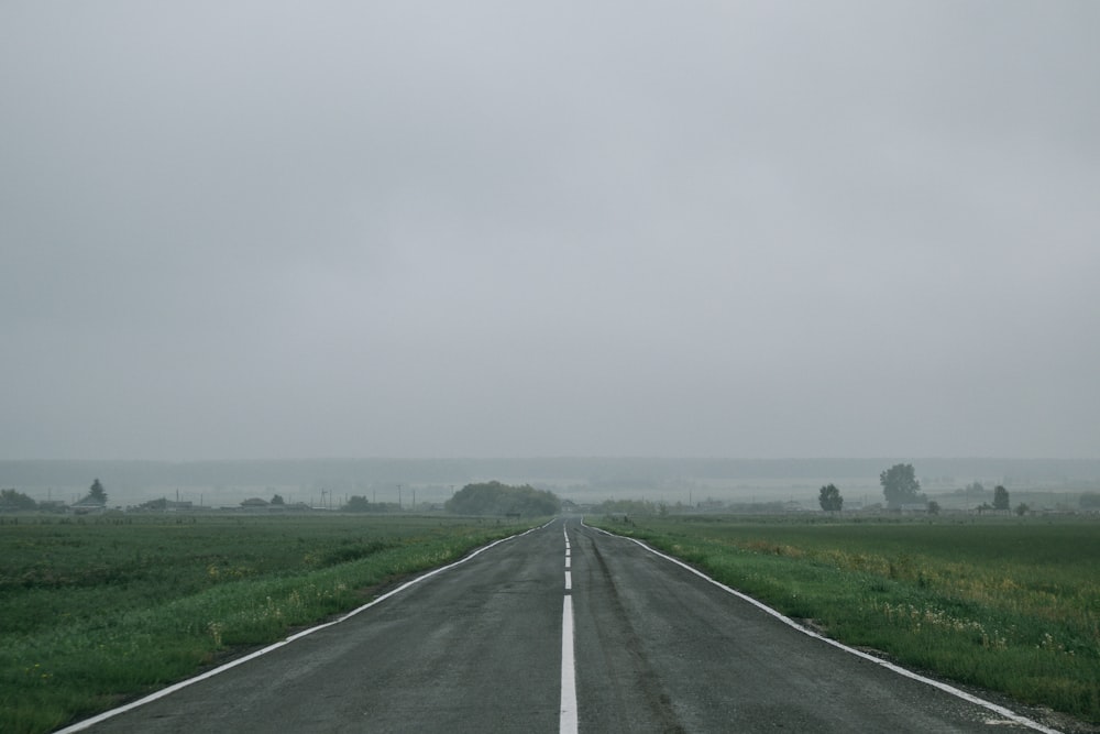 Carretera de asfalto gris entre campo de hierba verde bajo cielo blanco durante el día
