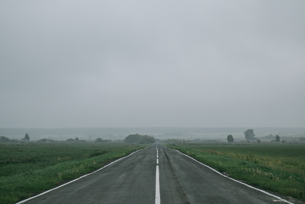 gray asphalt road between green grass field under white sky during daytime