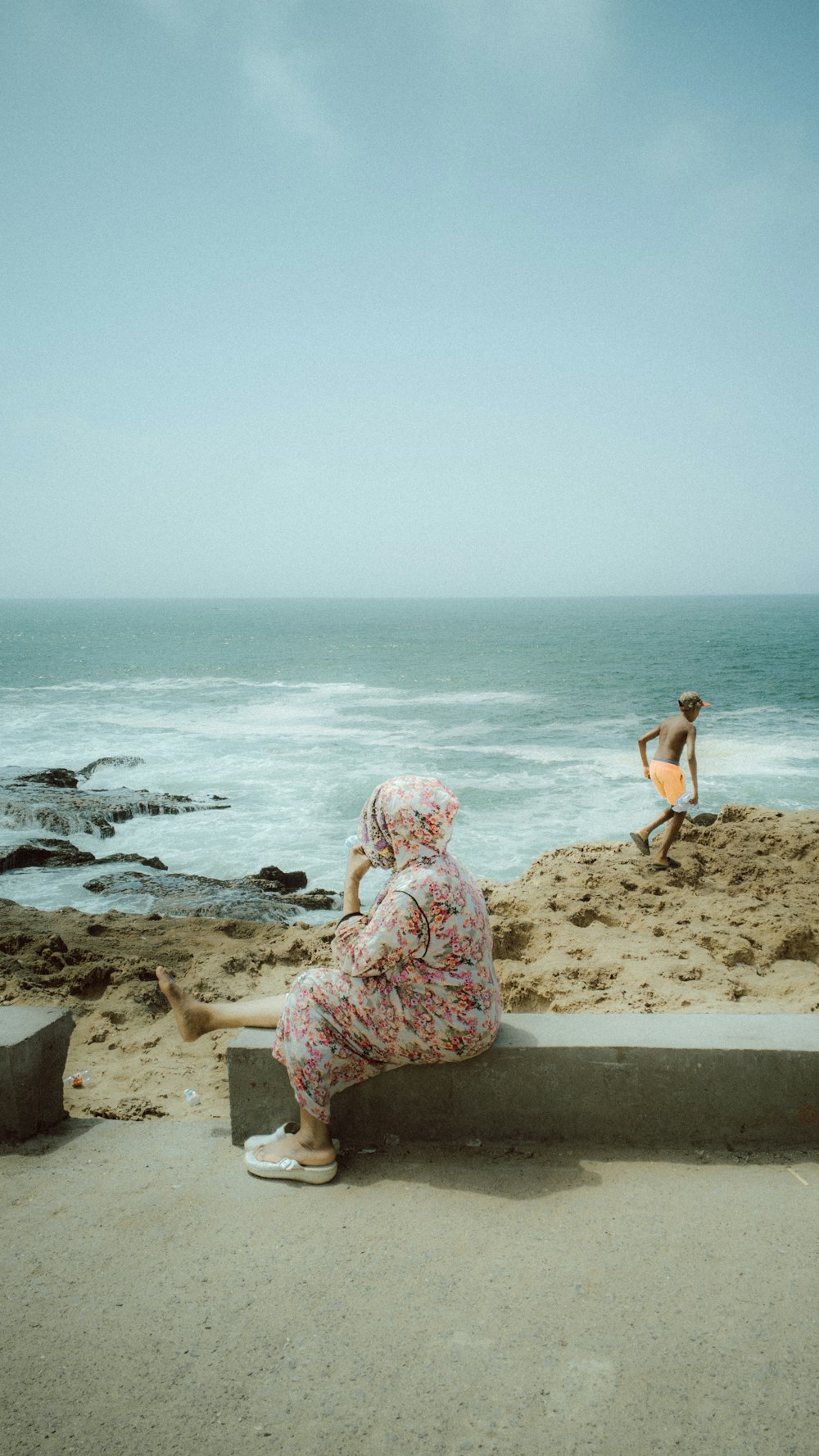 woman in white and pink floral dress sitting on brown sand near body of water during