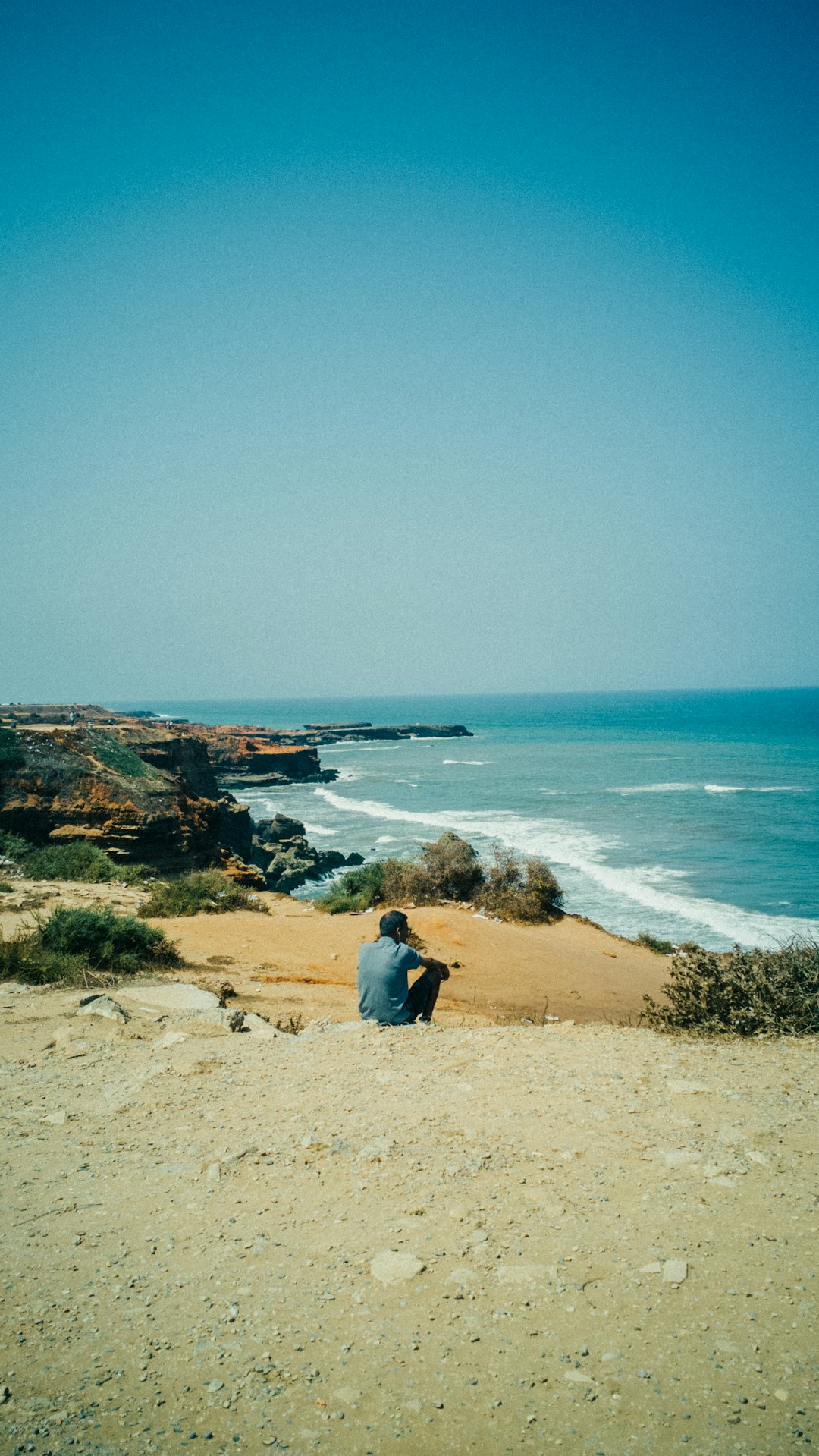 couple sitting on brown sand near body of water during daytime