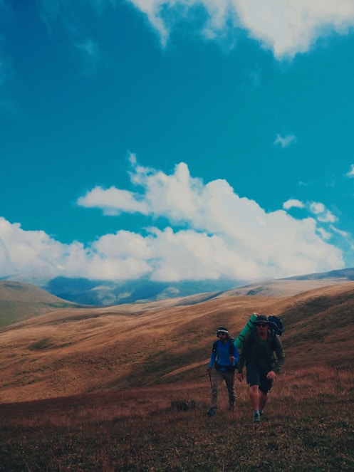 people hiking on brown mountain under blue sky and white clouds during daytime