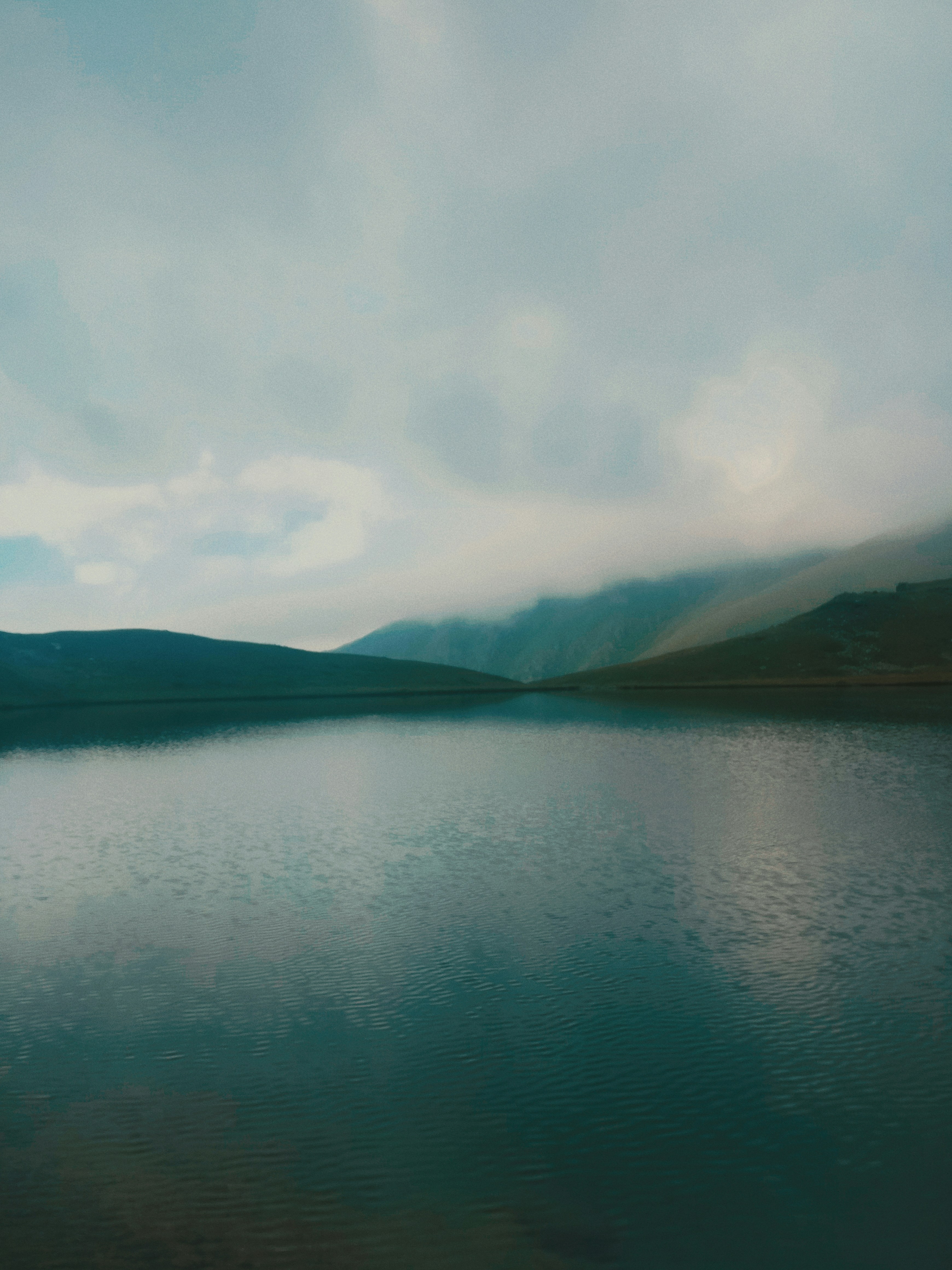 body of water near mountain under white clouds during daytime