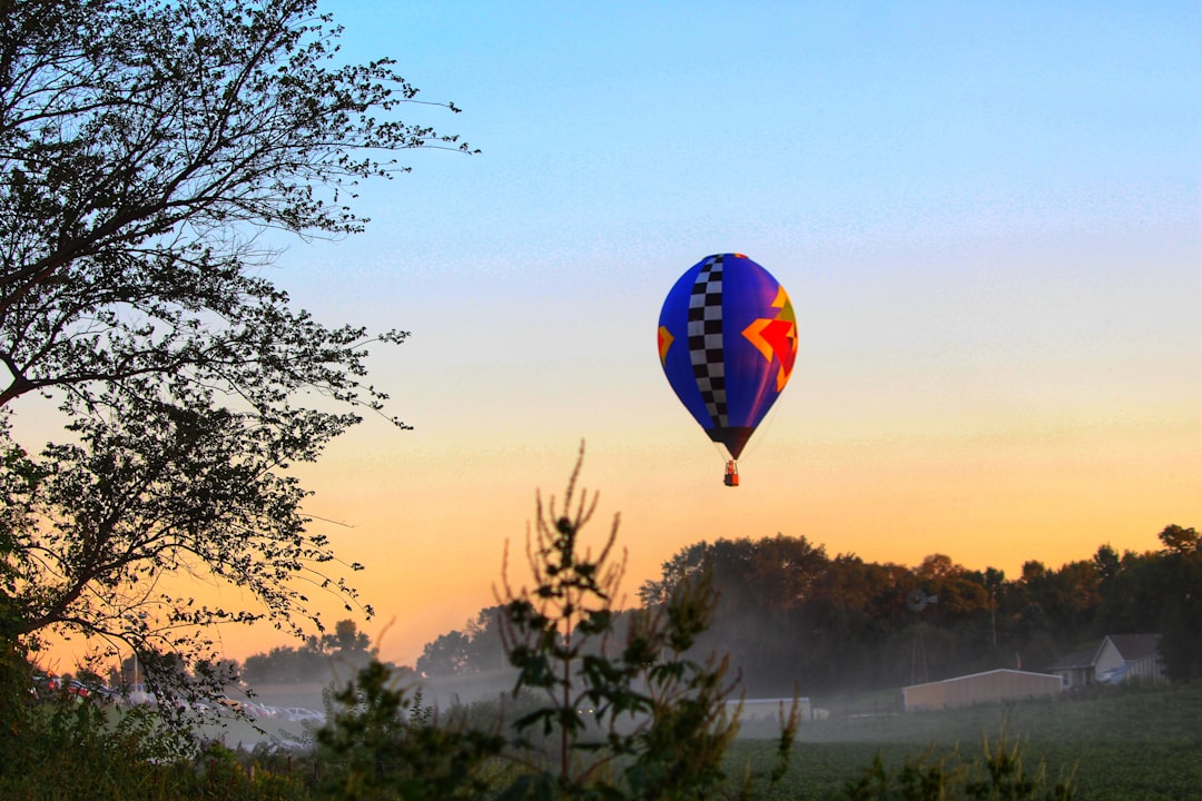 blue red and yellow hot air balloon flying over the trees during sunset