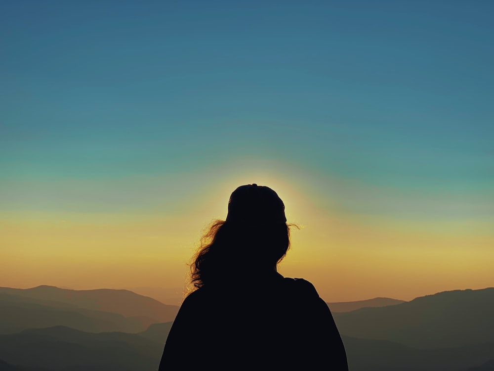 silhueta da mulher em pé no topo da montanha durante o pôr do sol
