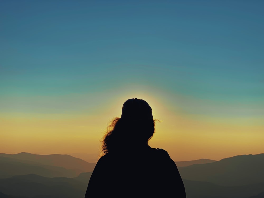 夕暮れ時の山頂に立つ女性のシルエット