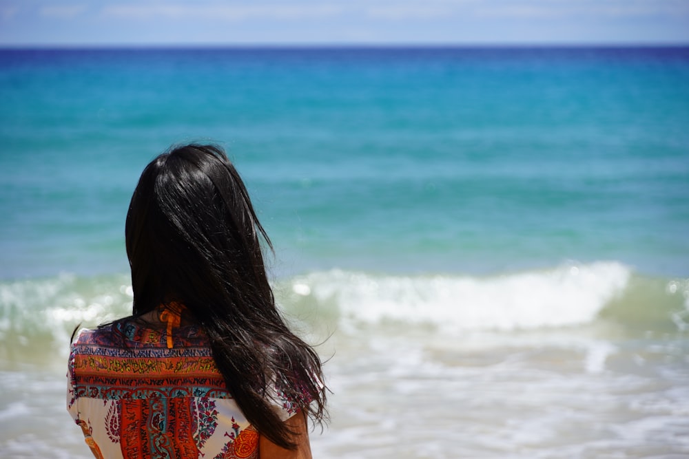 woman in red and white floral shirt standing by the sea during daytime