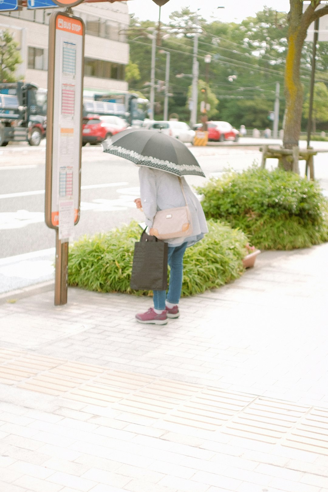 woman in white jacket and blue denim jeans holding umbrella walking on sidewalk during daytime