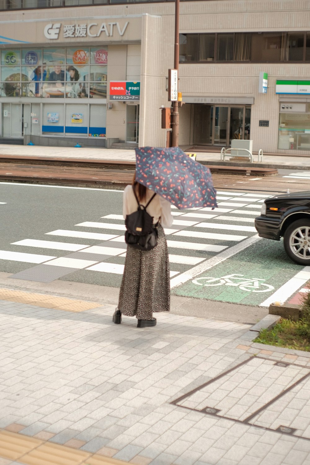 昼間に歩道を歩いて傘を保持している黒いコートを着た女性