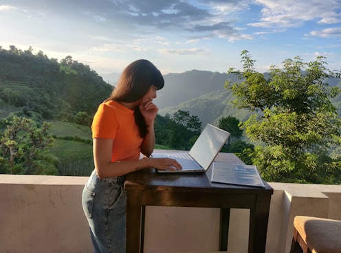 woman in orange shirt sitting on white chair reading book