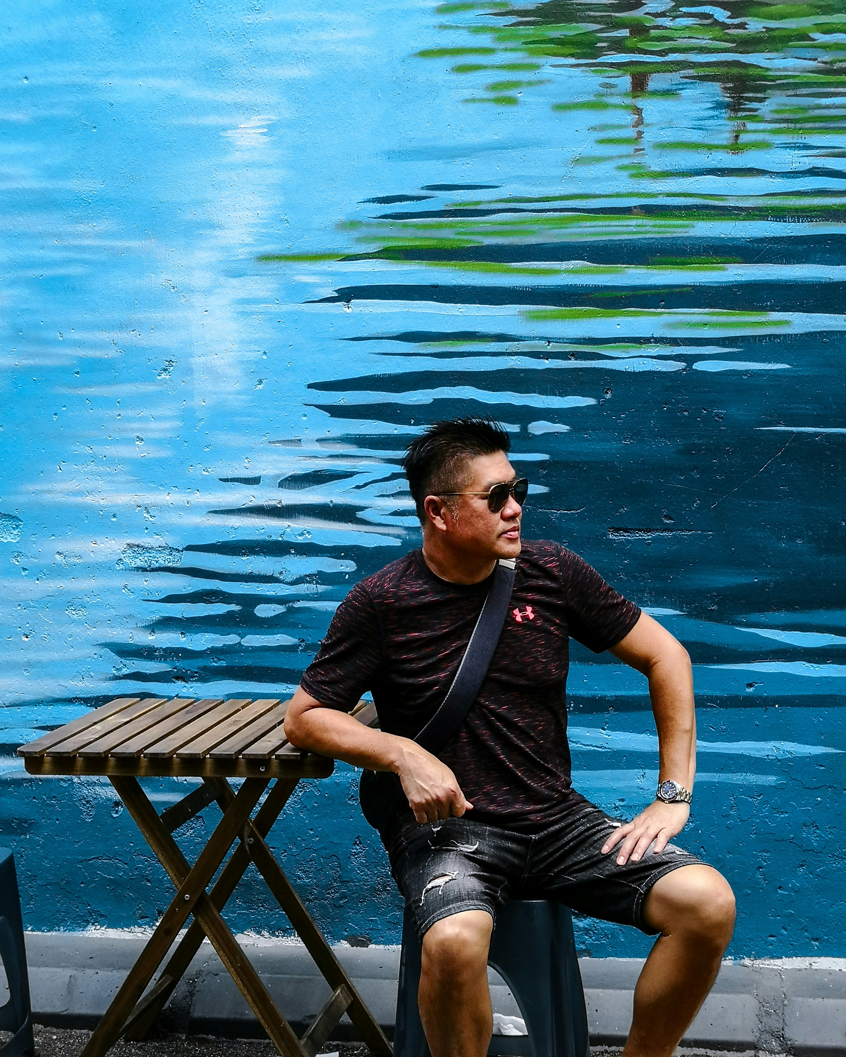 Pria dengan kaos hitam dan celana pendek denim biru duduk di kursi kayu coklat