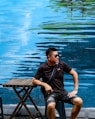 man in black t-shirt and blue denim shorts sitting on brown wooden chair