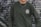A person is wearing a dark green sweatshirt with the logo 'Rehumanize International' printed on the chest. The background consists of a metal shutter with abstract graffiti patterns in shades of gray and purple. A chain necklace is worn around the neck.