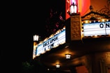 A vintage-style cinema marquee illuminated at night, displaying the words 'ONCE UPON A TIME'. The sign is adorned with classic light bulbs and ornate details. The warm glow of lanterns adds an old-fashioned charm to the scene, contrasting against the dark night sky.