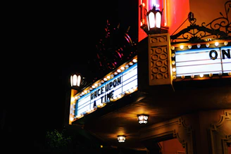 A warmly lit vintage movie marquee glowing against the evening sky at Nostalgia Lumière.
