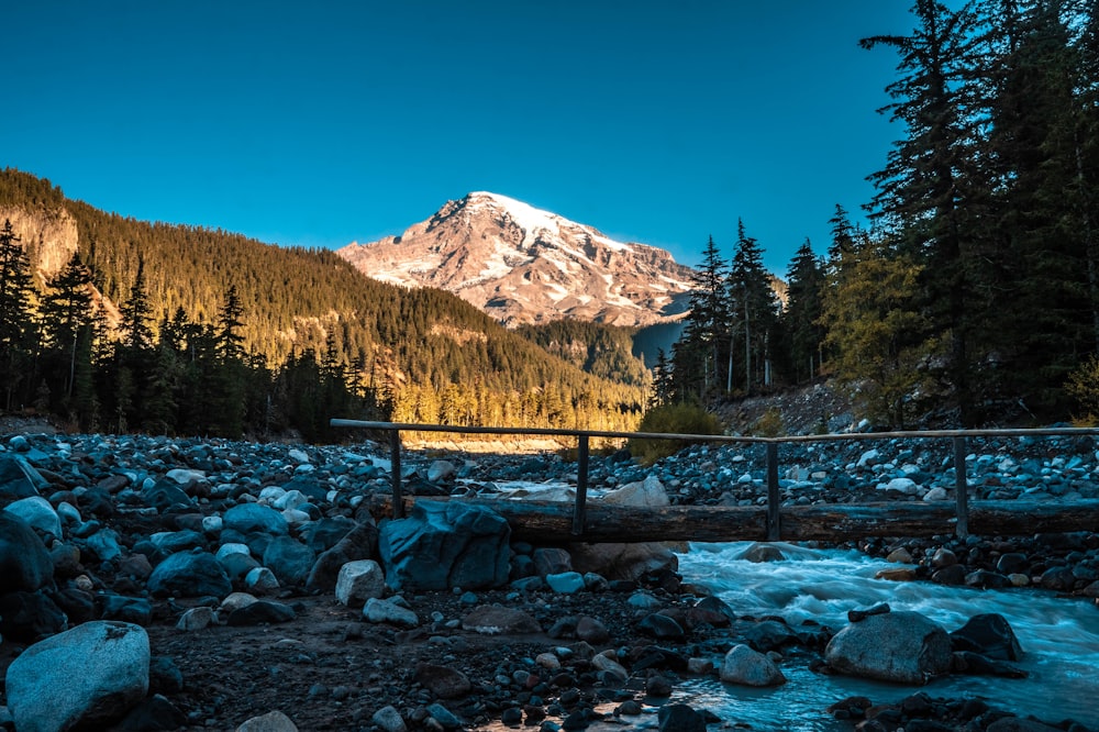 brown wooden bridge over river near snow covered mountain during daytime