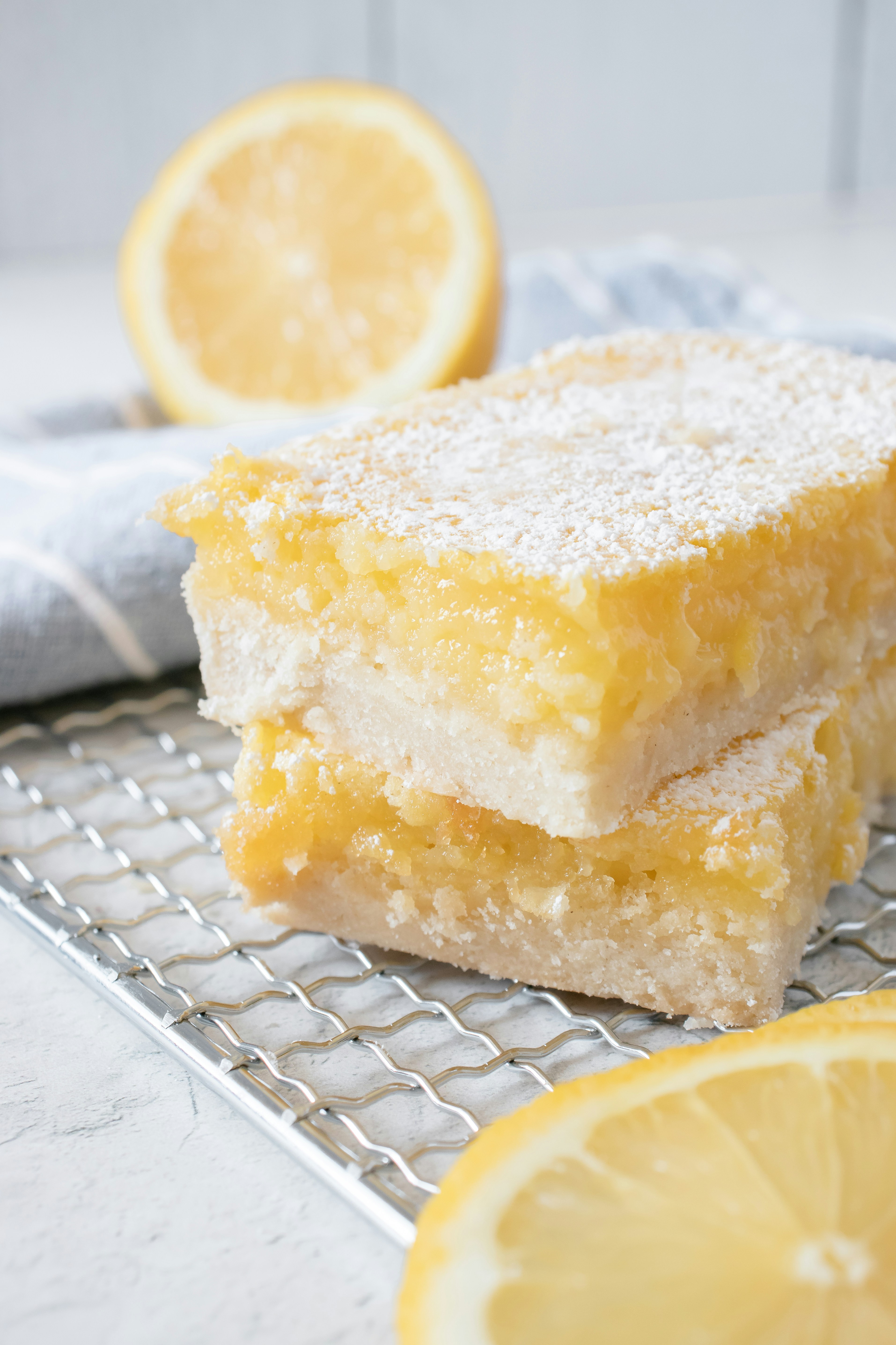 Two gluten-free lemon bars dusted with powdered sugar on a cooling rack