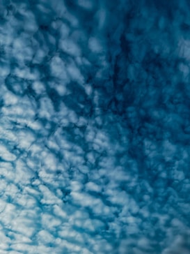 A cloud-filled sky with a textured pattern of fluffy, white clouds against a deep blue background. The clouds appear to be evenly distributed, creating an intricate and captivating visual effect.