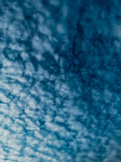 A cloud-filled sky with a textured pattern of fluffy, white clouds against a deep blue background. The clouds appear to be evenly distributed, creating an intricate and captivating visual effect.