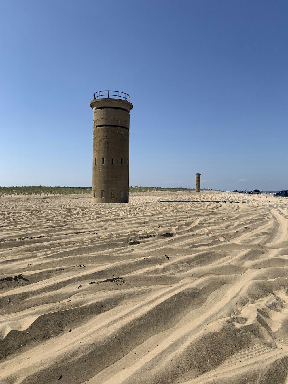 昼間の青空の下、茶色の砂浜に浮かぶ茶色のコンクリートの塔