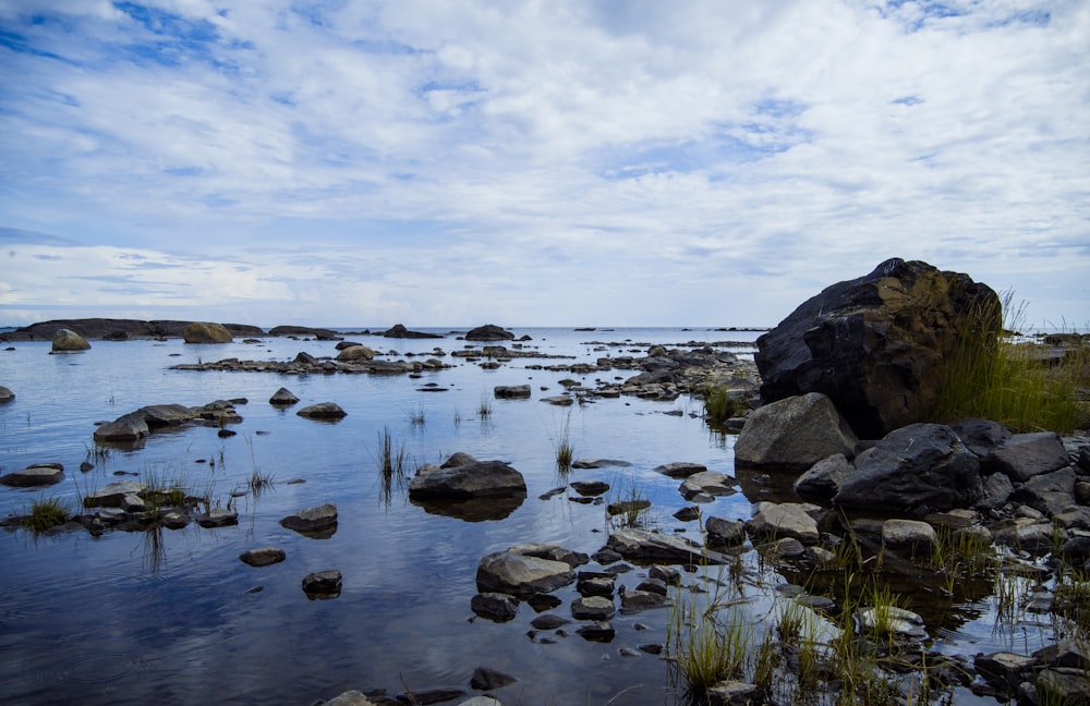 rocks on water under white clouds and blue sky during daytime