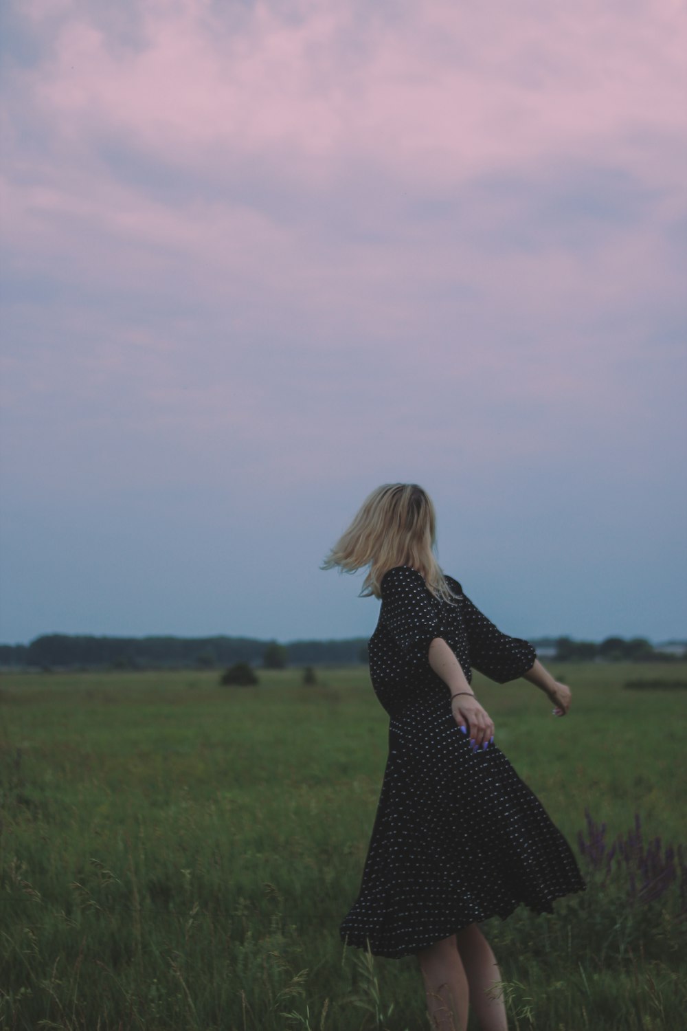 woman in black and white polka dot dress standing on green grass field during daytime