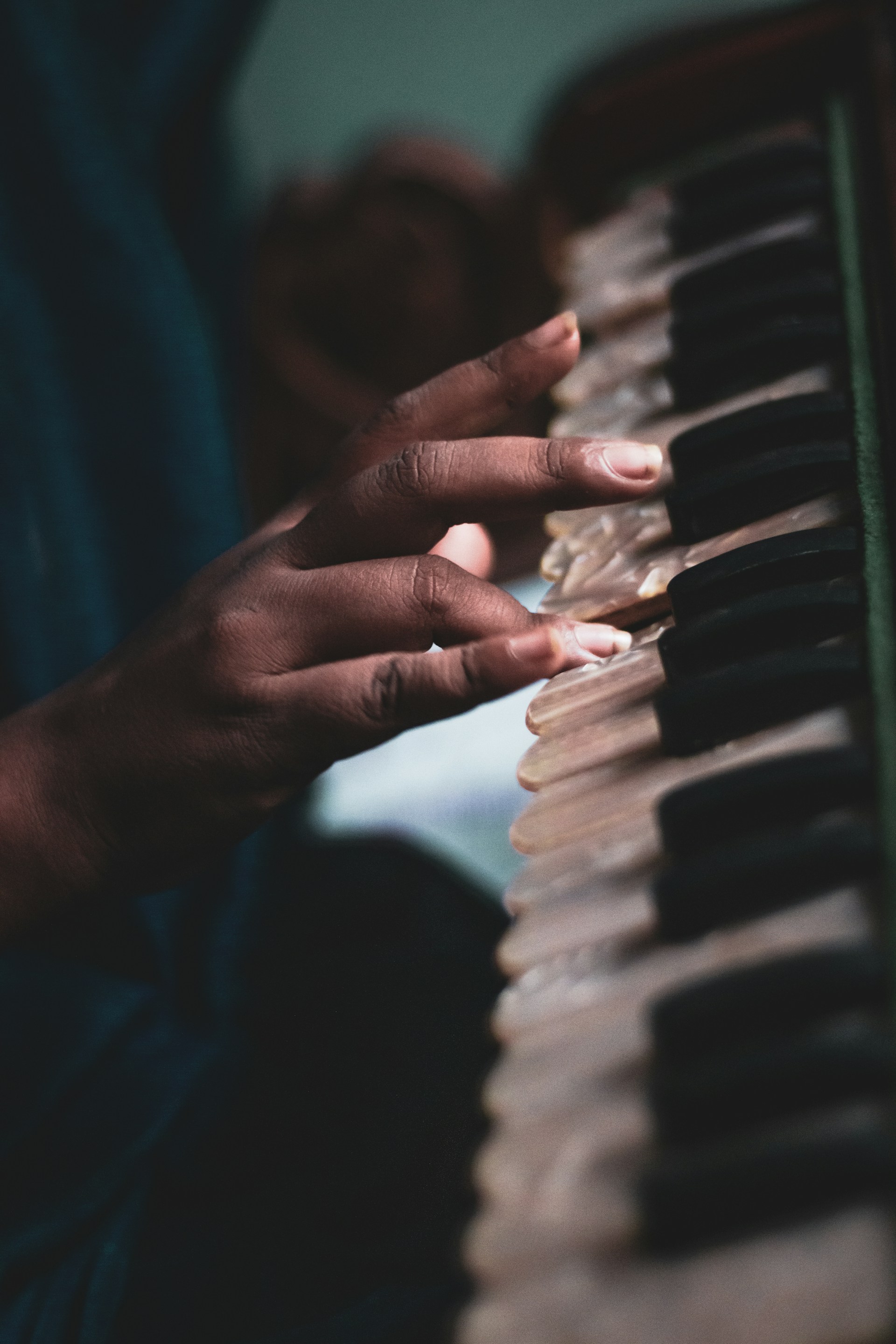 Close-up of hands playing a harmonium with soft golden light highlighting the intricate details of the instrument.