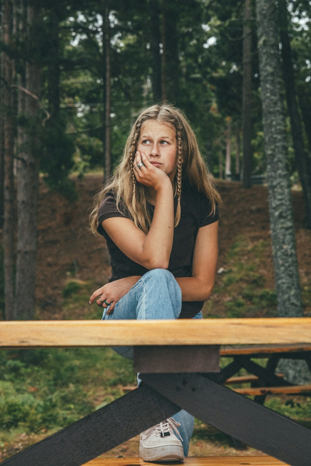 woman in black tank top and blue denim jeans sitting on brown wooden bench
