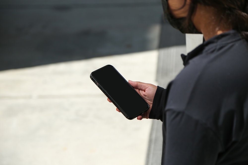 uomo in camicia nera che tiene lo smartphone nero