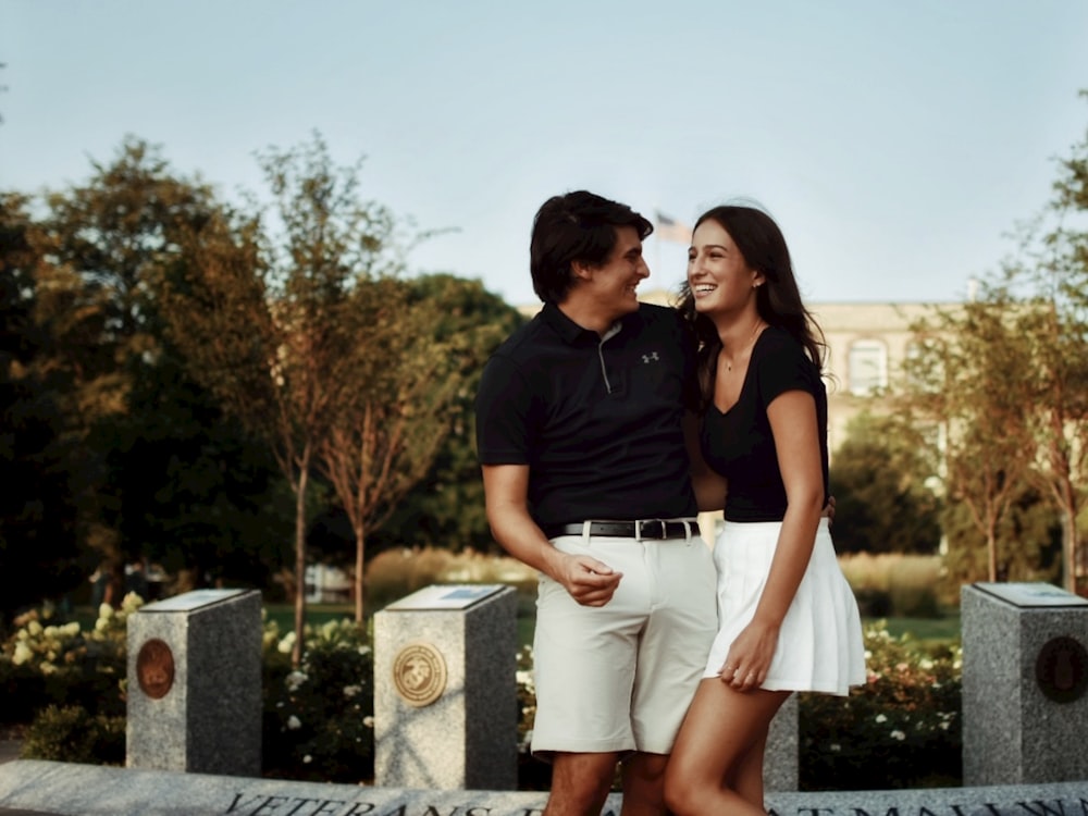 man in black polo shirt and white shorts standing beside woman in white skirt during daytime