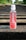 A bottle of Karma Probiotic Water with a berry cherry flavor is placed on wooden railroad tracks. The background features lush green foliage alongside the tracks, giving a sense of depth and perspective.