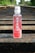A bottle of Karma Probiotic Water with a berry cherry flavor is placed on wooden railroad tracks. The background features lush green foliage alongside the tracks, giving a sense of depth and perspective.
