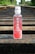 A bottle of Karma Probiotic Water with a berry cherry flavor is placed on wooden railroad tracks. The background features lush green foliage alongside the tracks, giving a sense of depth and perspective.
