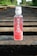 A bottle of Karma Probiotic Water with a berry cherry flavor is placed on wooden railroad tracks. The background features lush green foliage alongside the tracks, giving a sense of depth and perspective.