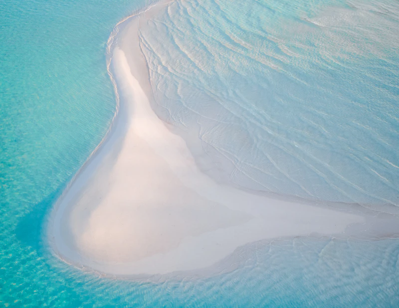 A curved white sandbar in pale turquoise shallows off Saddle Back Cay in the Exumas
