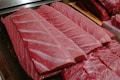 Several thick, rectangular slices of raw fish, likely tuna, displayed on a wooden board. The flesh has a rich, pinkish-red color with visible marbling and a moist, fresh appearance.