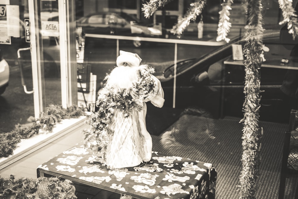 창문 근처에 서 있는 하얀 드레스를 입은 여자의 회색조 사진