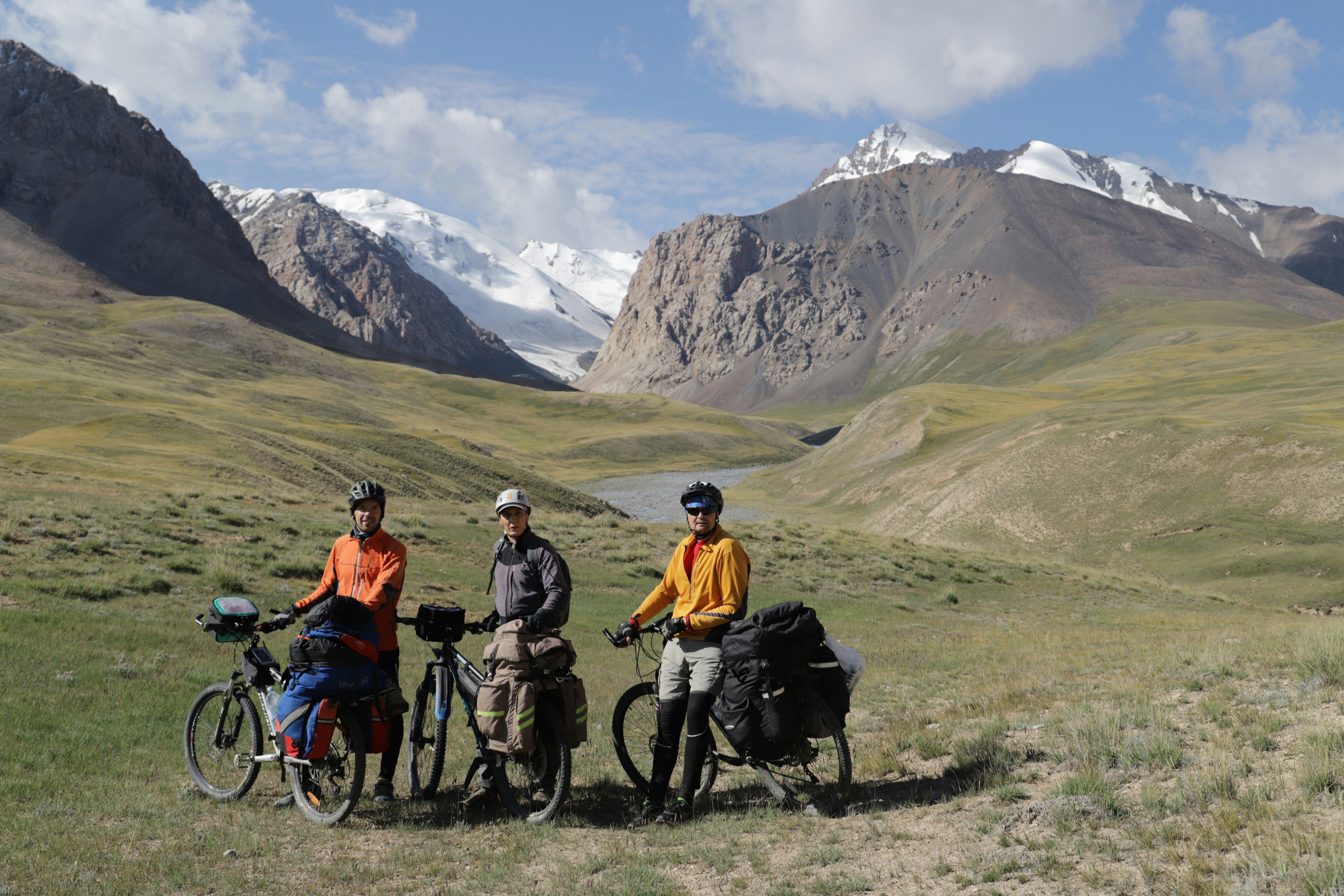 2 men riding bicycles on green grass field near snow covered mountain during daytime